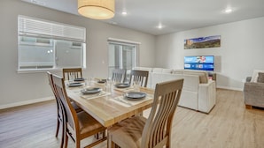 A modern living room with a dining area, a flat-screen TV, and a large window with blinds. - Top Flight (Colorado Springs)