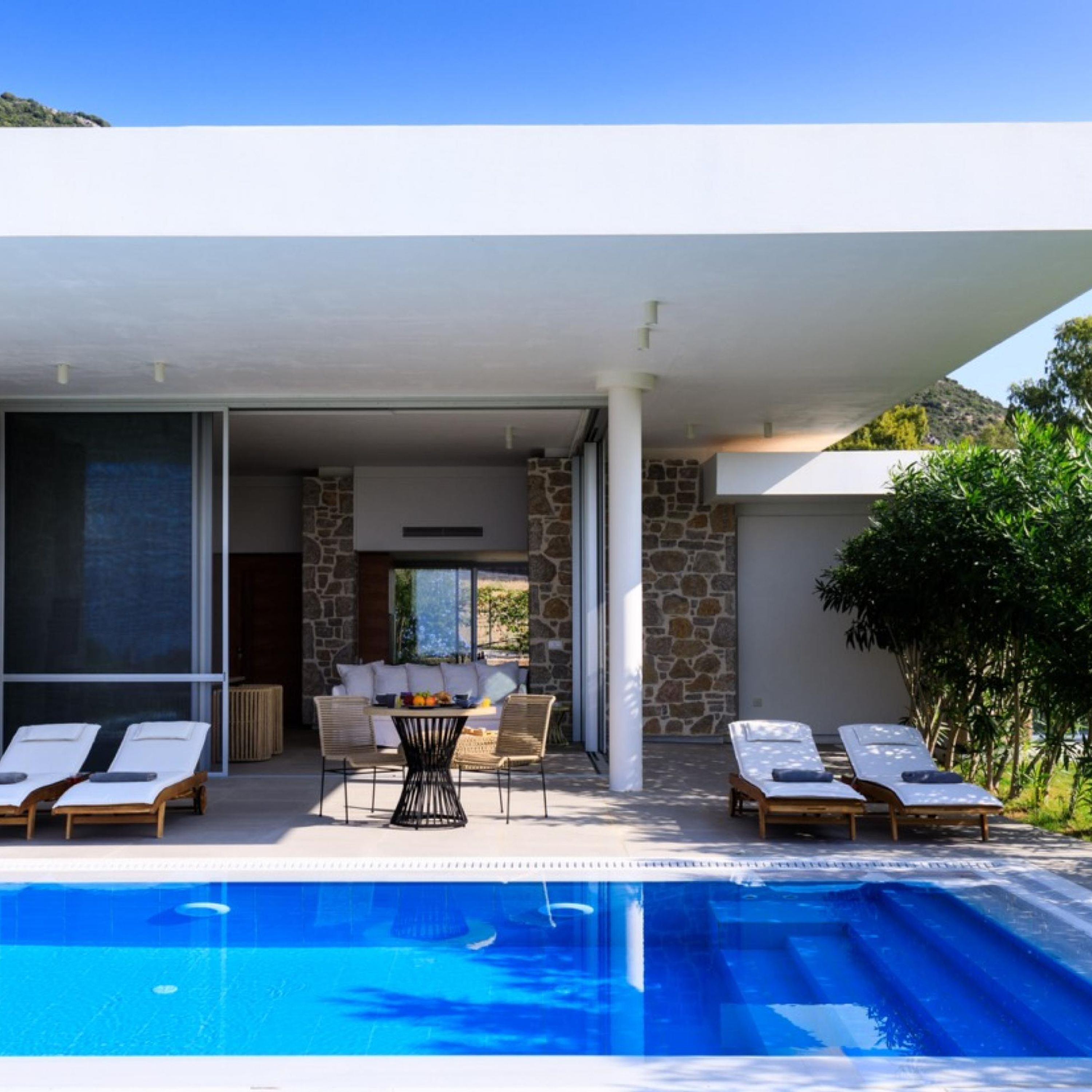 Un área de piscina moderna al aire libre con sillones de descanso y una mesa de comedor.