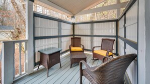 A covered porch with wicker furniture and a table, featuring a view of trees and a house in the background. - Spacious Mooresville Home w/ Lake Norman View! (Mooresville)