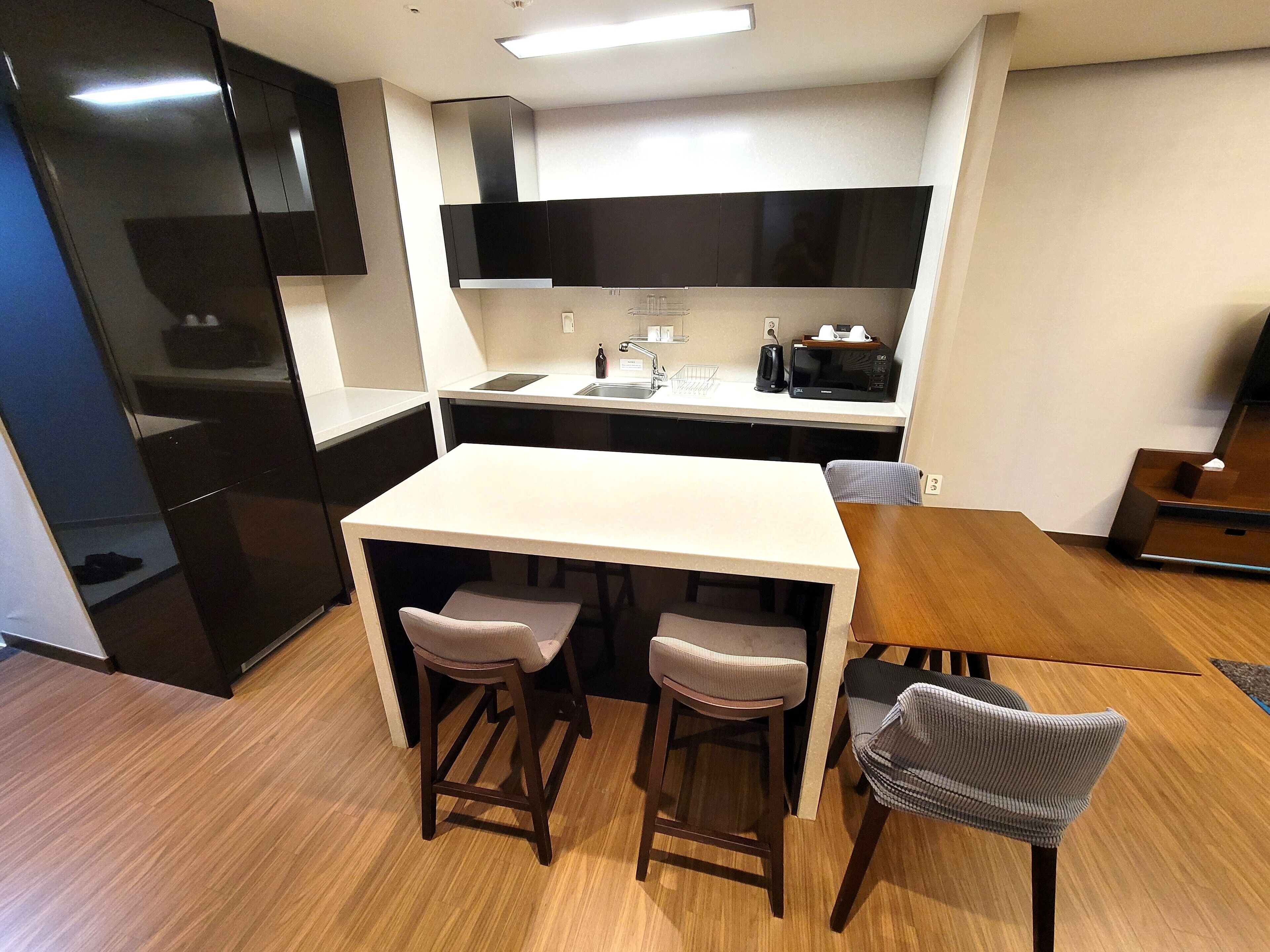 A compact kitchen with a central island, bar stools, and a microwave.