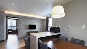 A modern hotel room with a wooden dining table, a flat-screen TV mounted on the wall, and a large window offering a view of the outside. - W Residence Hotel Haeundae (Busan)