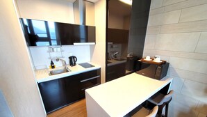 A compact kitchen with a white countertop, black cabinets, and a wooden floor. - W Residence Hotel Haeundae (Busan)