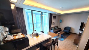 A modern hotel room with a kitchen area, a dining table, a sofa, and a large window offering a city view. - W Residence Hotel Haeundae (Busan)