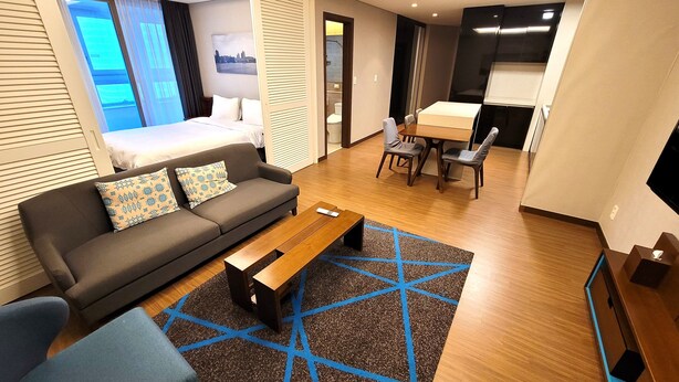 A modern hotel room with a sofa, a coffee table, a dining area with chairs, and a view of the city through the window. - W Residence Hotel Haeundae (Busan)