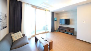 A modern living room with a sofa, a coffee table, a flat-screen TV mounted on the wall, and a sliding glass door leading to an outdoor area. - W Residence Hotel Haeundae (Busan)