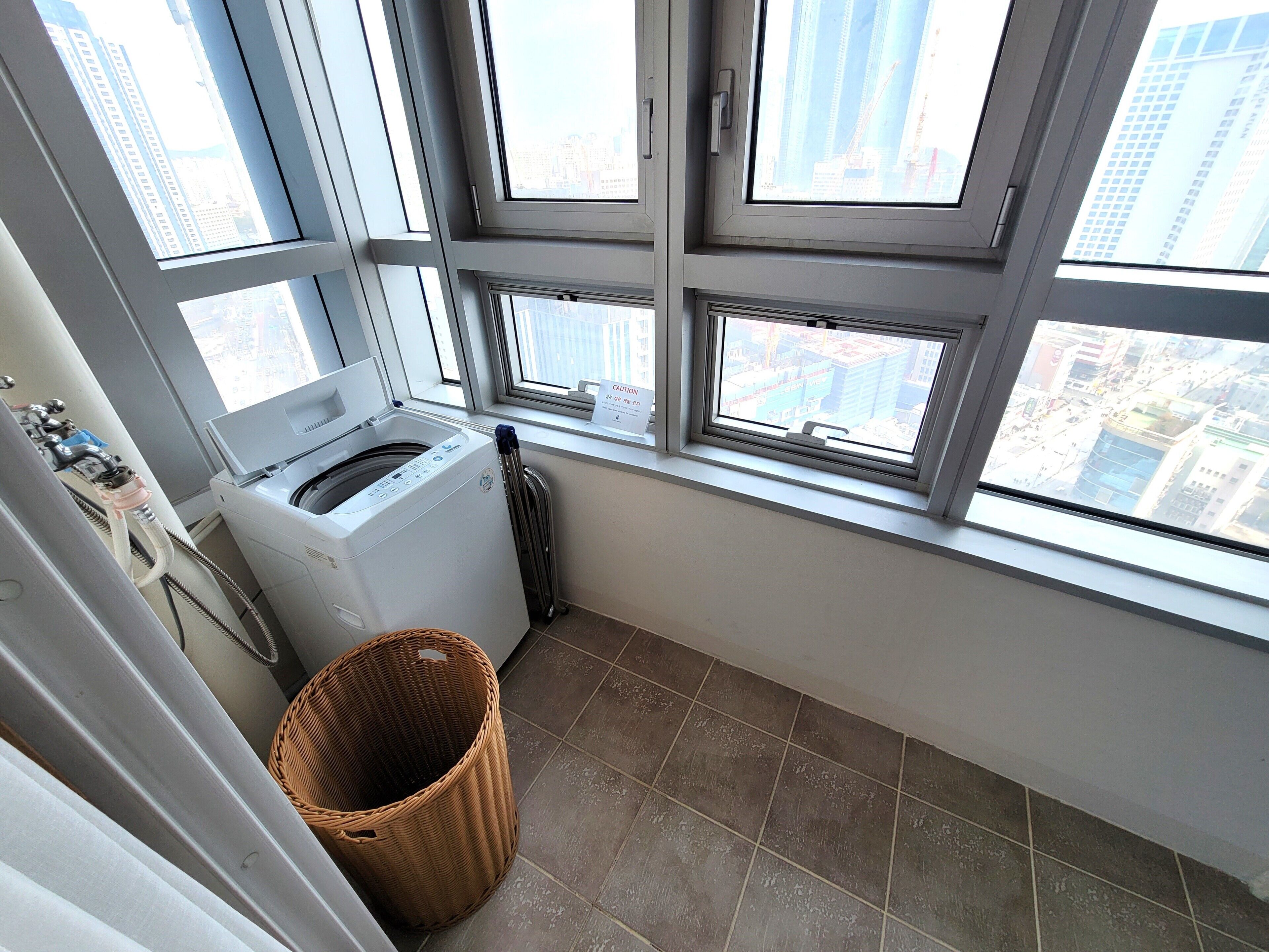 A laundry room with a front-loading washer and dryer, a wicker basket, and a view of the city through large windows.