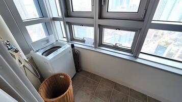 A laundry room with a front-loading washer and dryer, a wicker basket, and a view of the city through large windows.