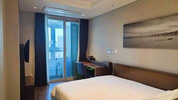 A hotel room with a bed, a desk, a TV, and a view of a cityscape through the window.