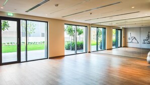 A spacious indoor area with large sliding glass doors leading to a garden, wooden flooring, and a wall with yoga silhouettes.