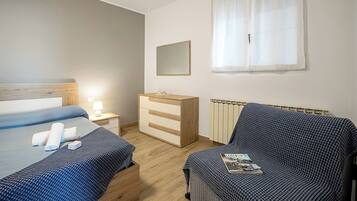 A bedroom with a bed, a dresser, a nightstand, a window with curtains, and a radiator.