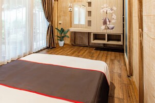 Habitación de hotel con una cama grande, suelo de madera, una planta en maceta y un espejo sobre un aparador de madera.