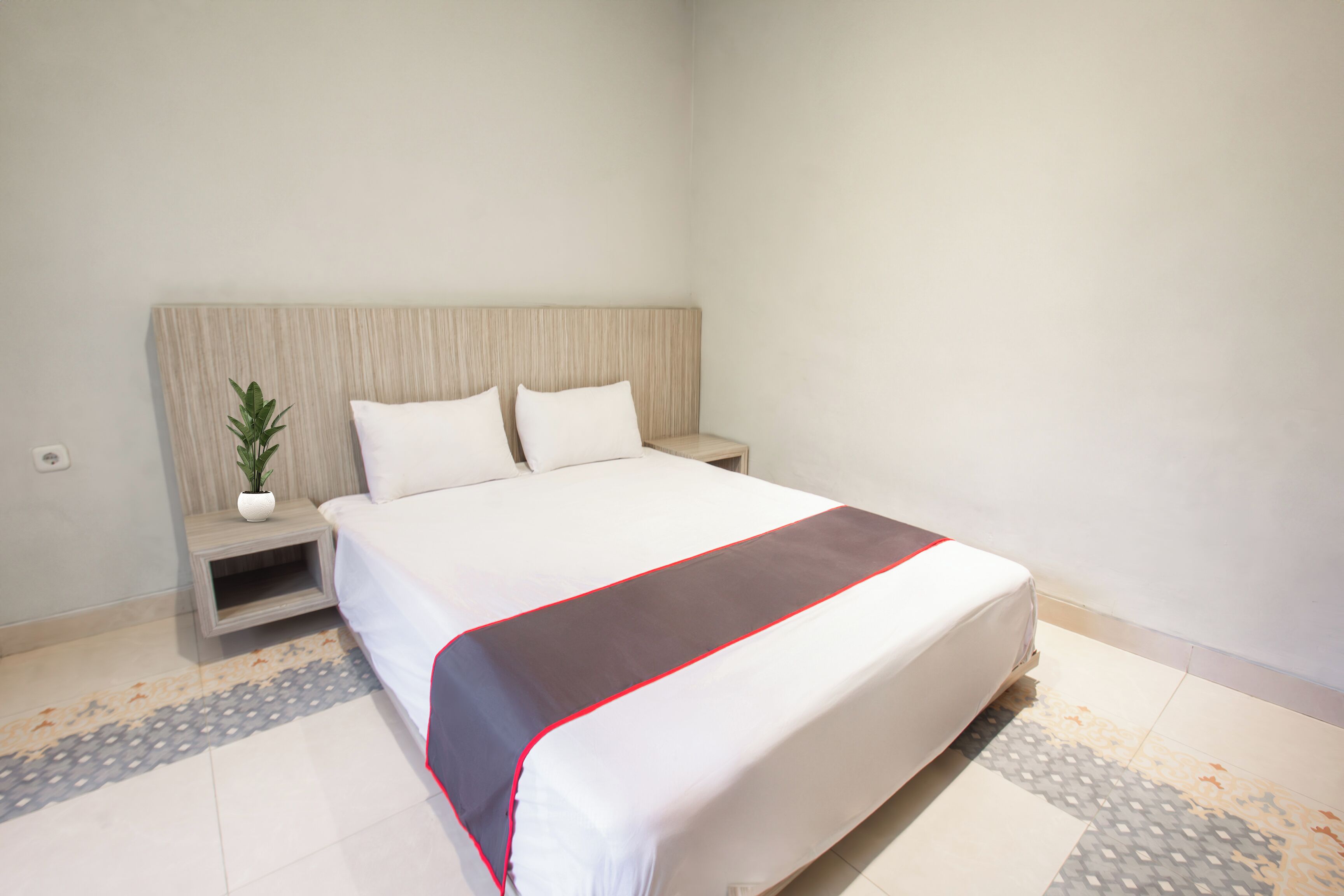 Quarto de hotel com uma cama grande, mesa de cabeceira com uma planta e chão estampado.
