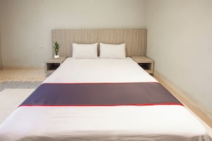 Una cama bien hecha con una colcha blanca y oscura, dos almohadas y un cabecero de madera.