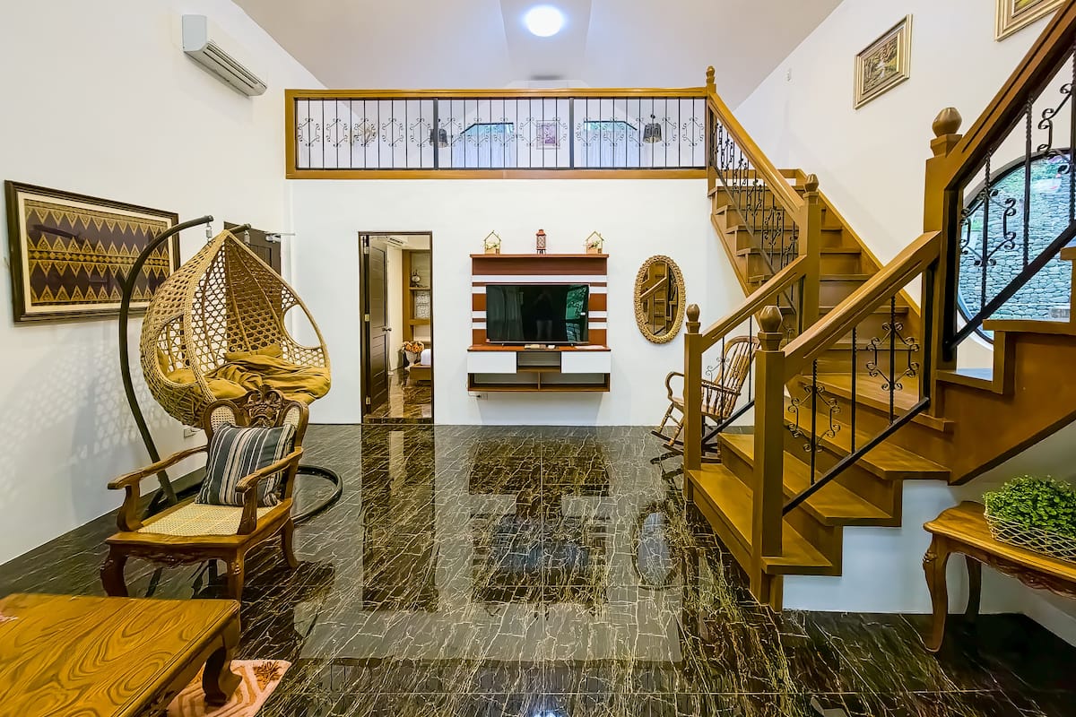 A spacious living area with a high ceiling, a wooden staircase, and a modern entertainment unit.