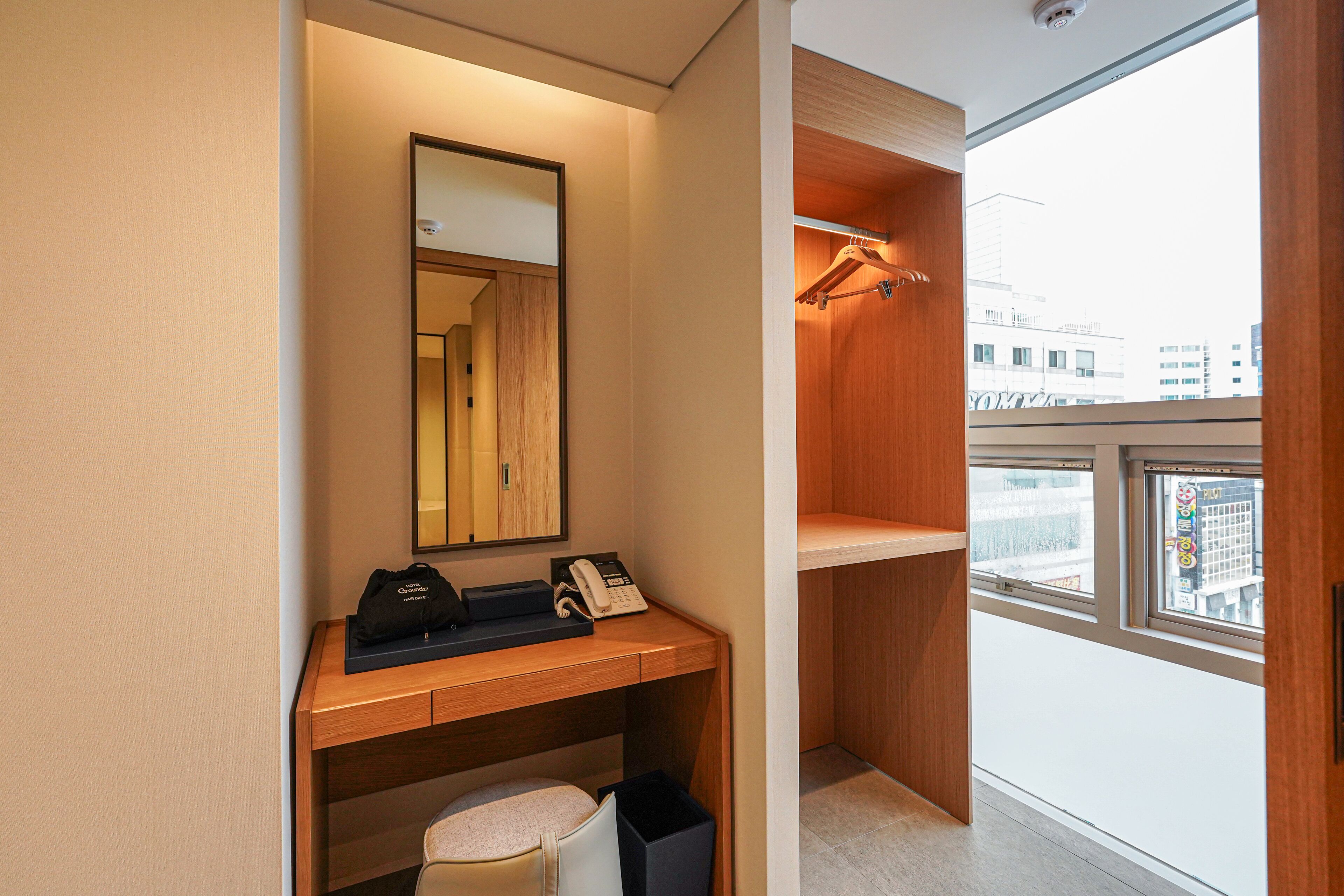 Una habitación de hotel moderna con un escritorio de madera, un teléfono, un bolso y un espejo.