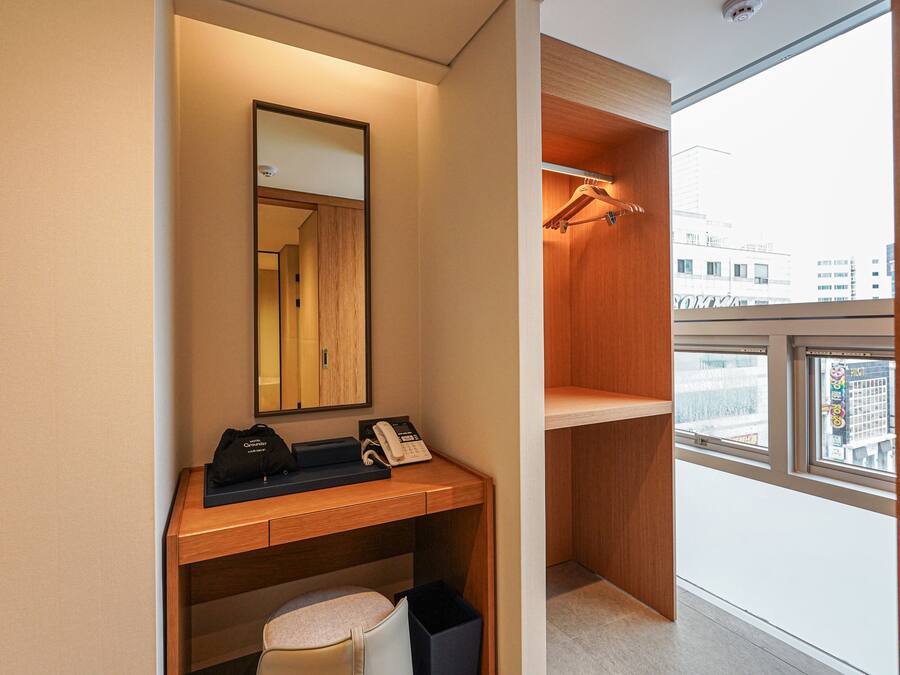 Una habitación de hotel moderna con un escritorio de madera, un teléfono, un bolso y un espejo.