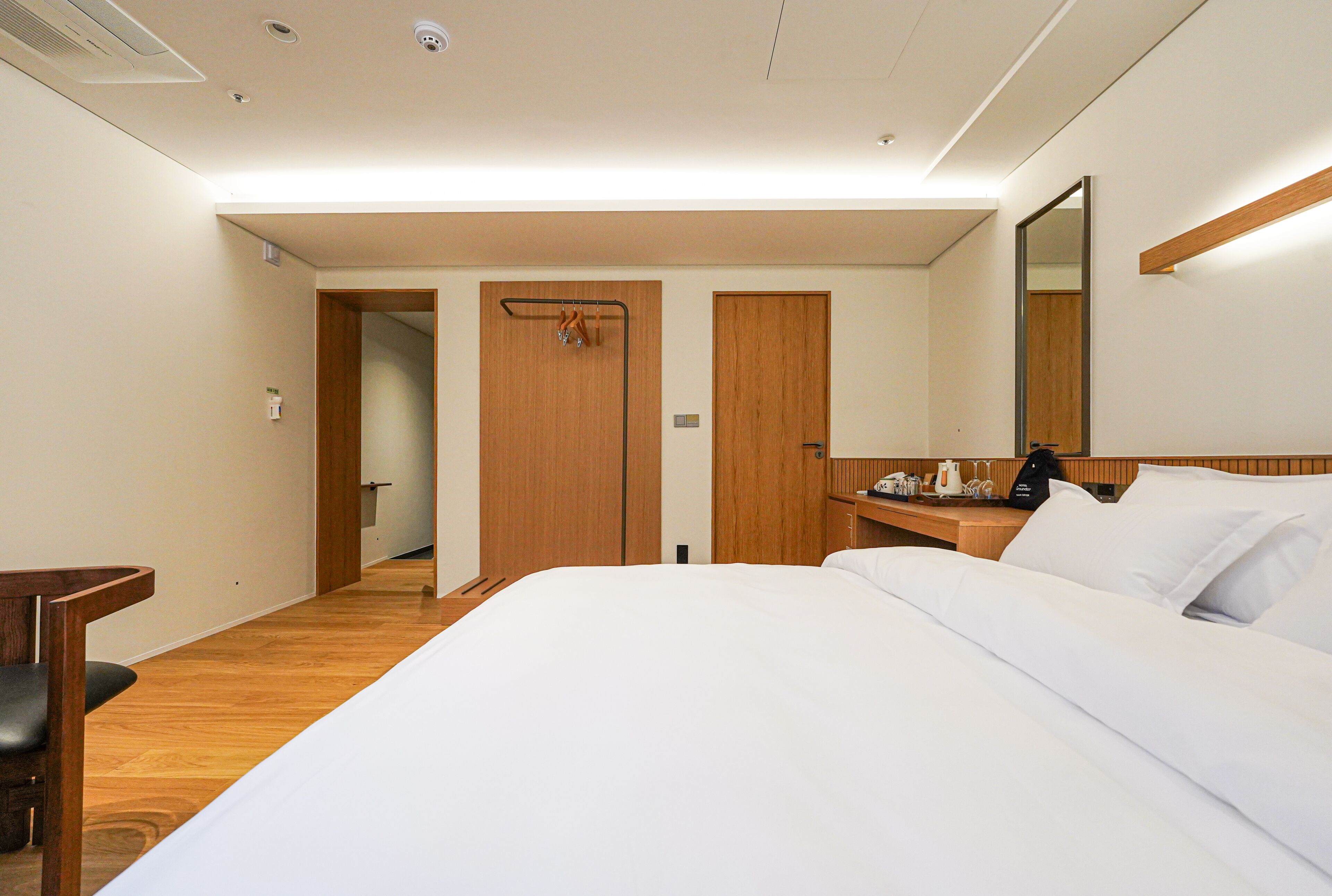 A hotel room with a large bed, wooden flooring, a wooden wardrobe, a bedside table with a lamp, and a mirror on the wall.