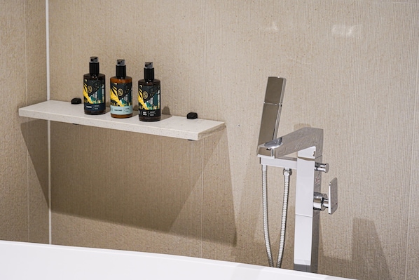 A bathroom with a shower and a shelf holding three bottles.