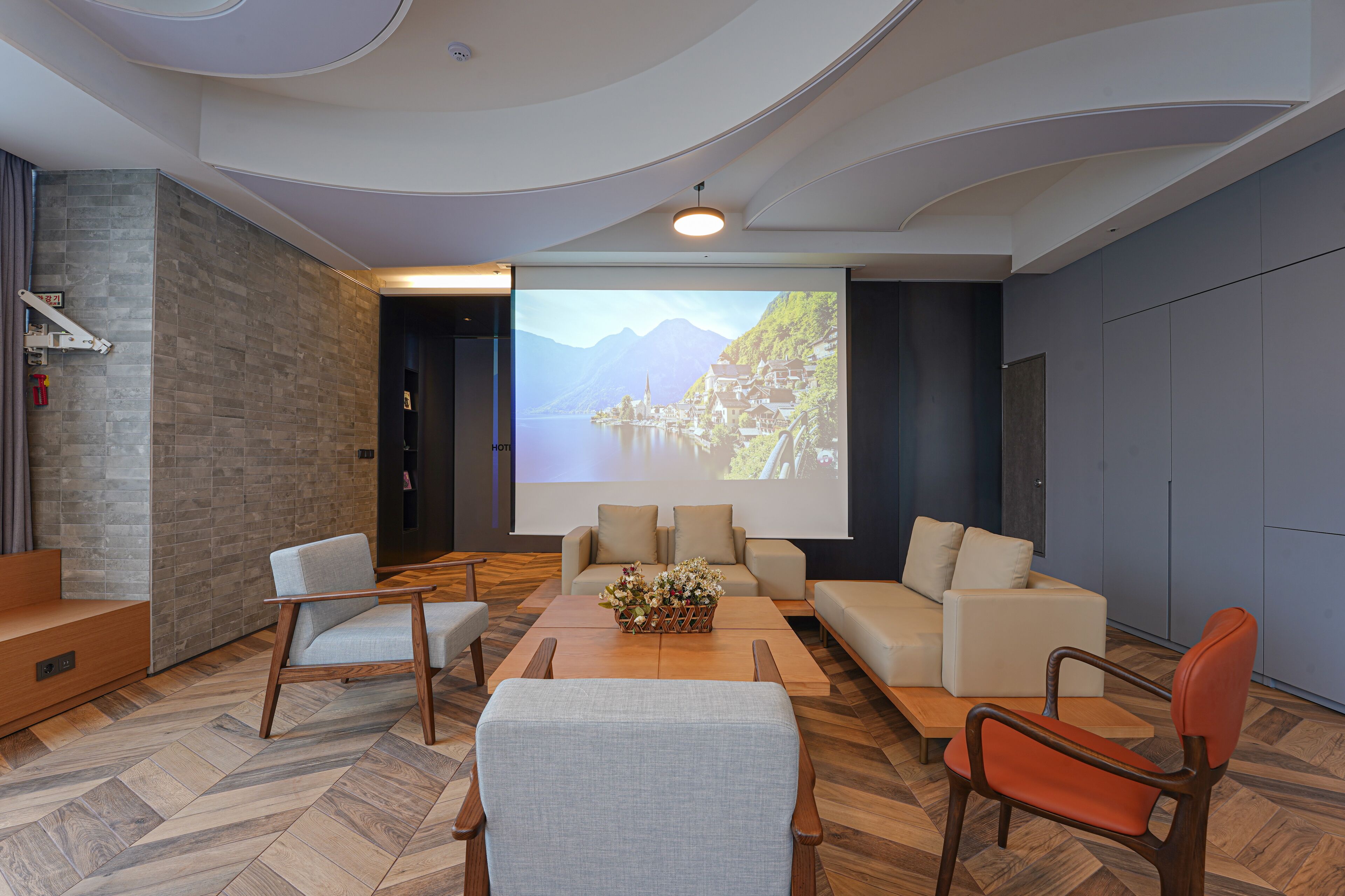 Una sala de estar moderna con una pantalla grande que muestra una vista panorámica, asientos cómodos y un suelo con patrón de espiga.