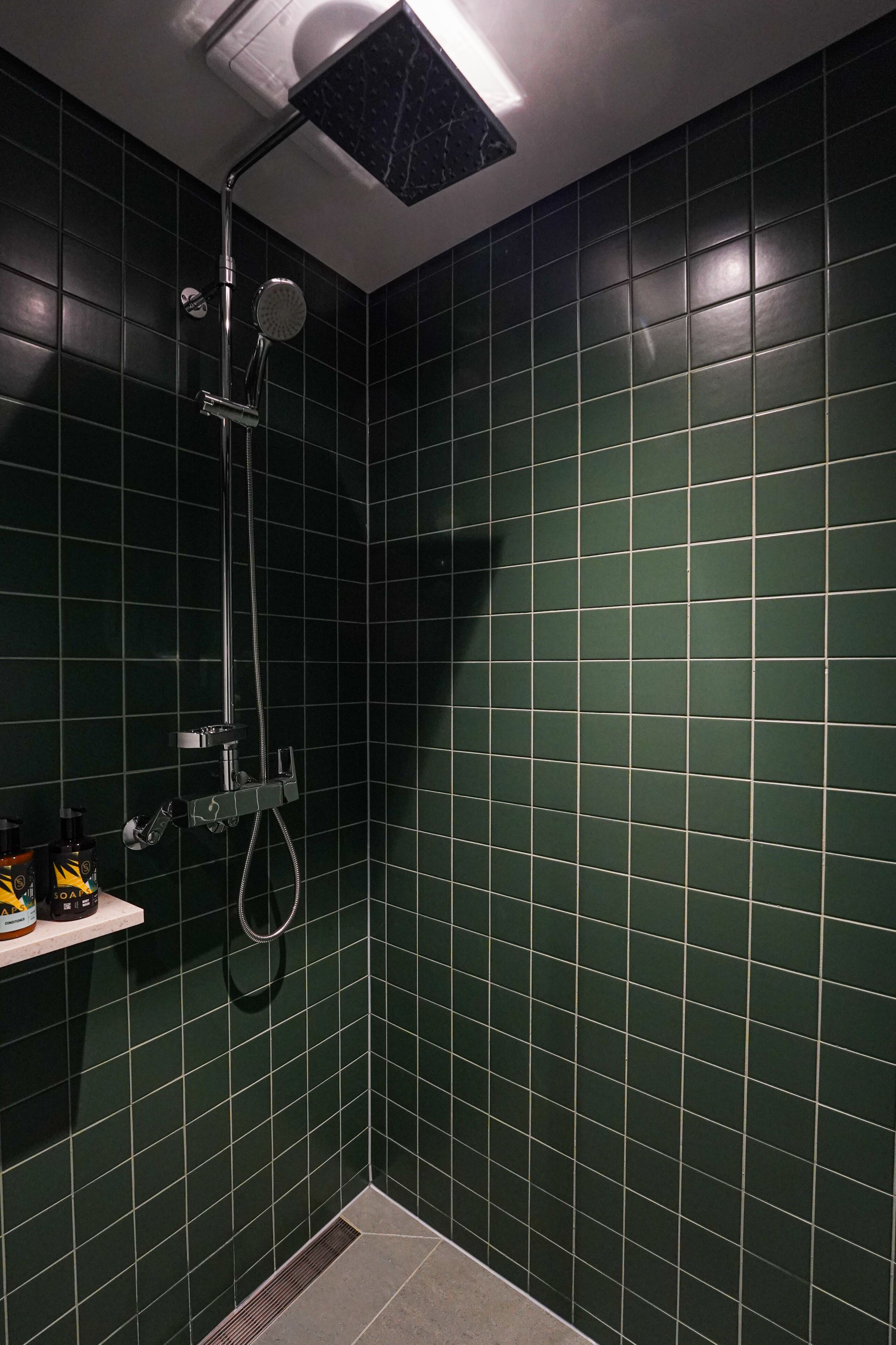 A small, dark green-tiled shower area with a handheld showerhead and a wall-mounted faucet.