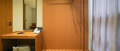 A hotel room with a wooden desk, a telephone, a mirror, and a hanging coat rack.