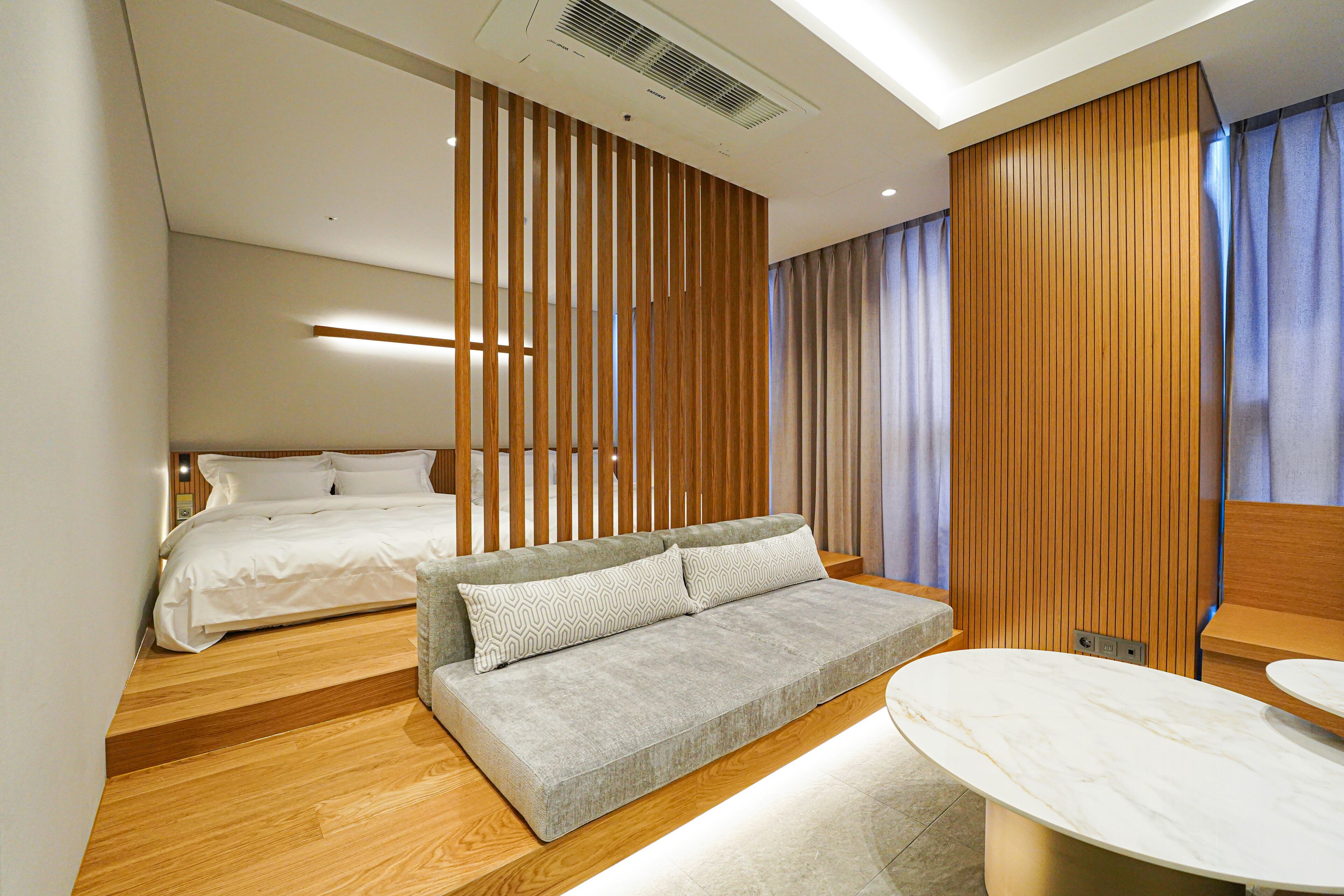 A modern hotel room with a sofa, a bed, a small table, and a wooden partition.