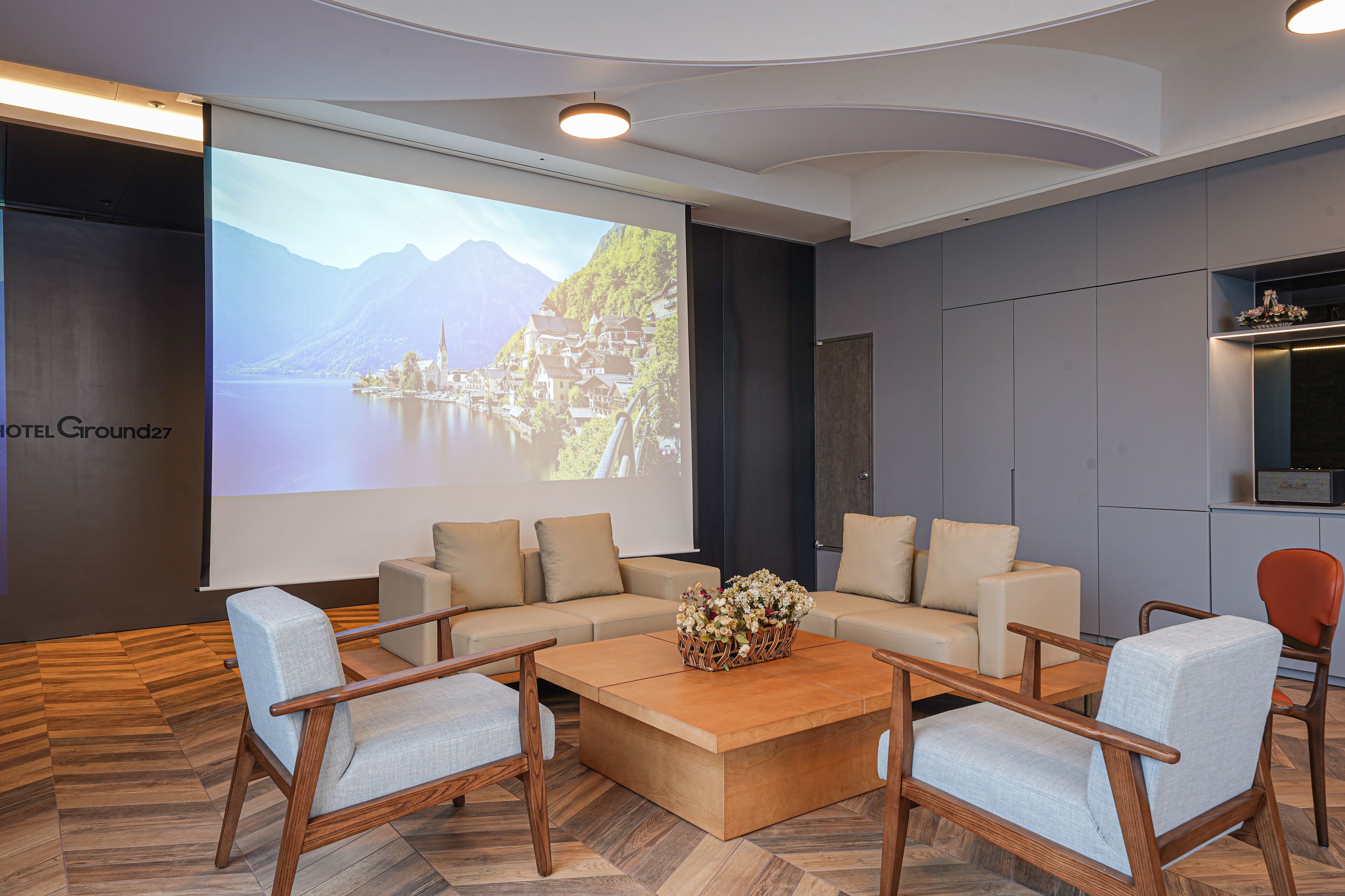 A modern hotel lobby with a large screen displaying a scenic view, comfortable seating, and a wooden coffee table.