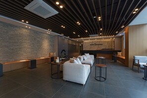 A modern hotel lobby with a reception desk, seating area, and a large wall with the hotel name.