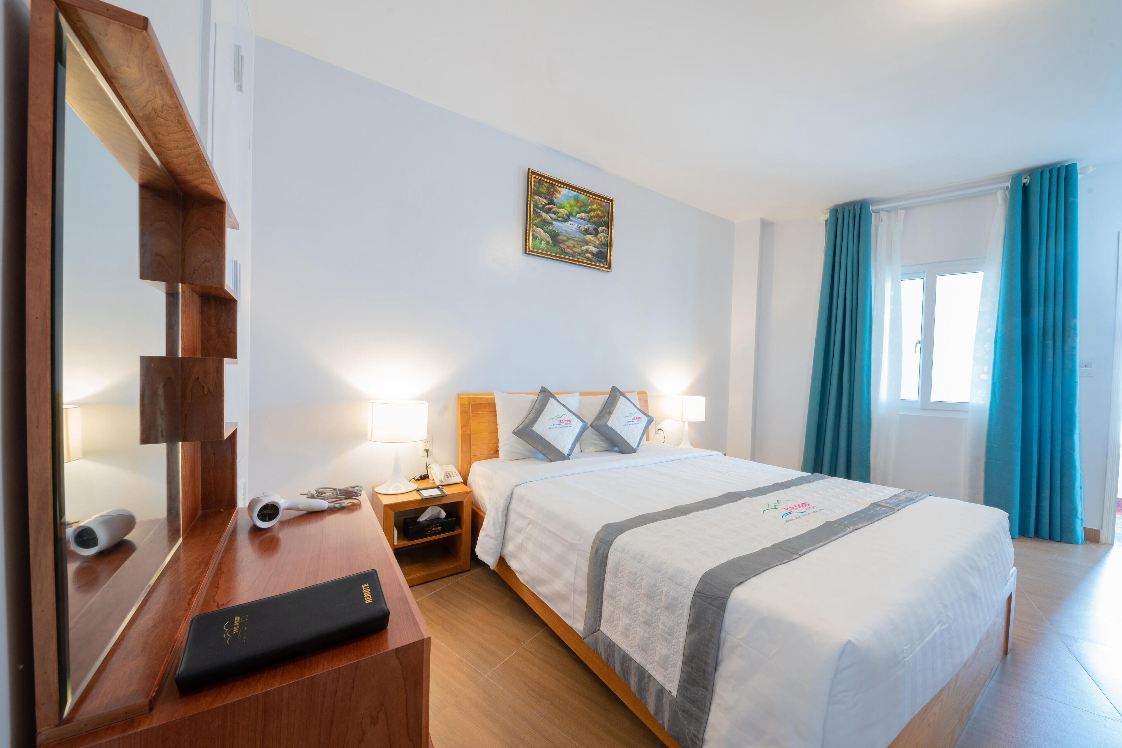 Une chambre d’hôtel avec un lit, un bureau, un miroir, une table de chevet et un tableau au mur.