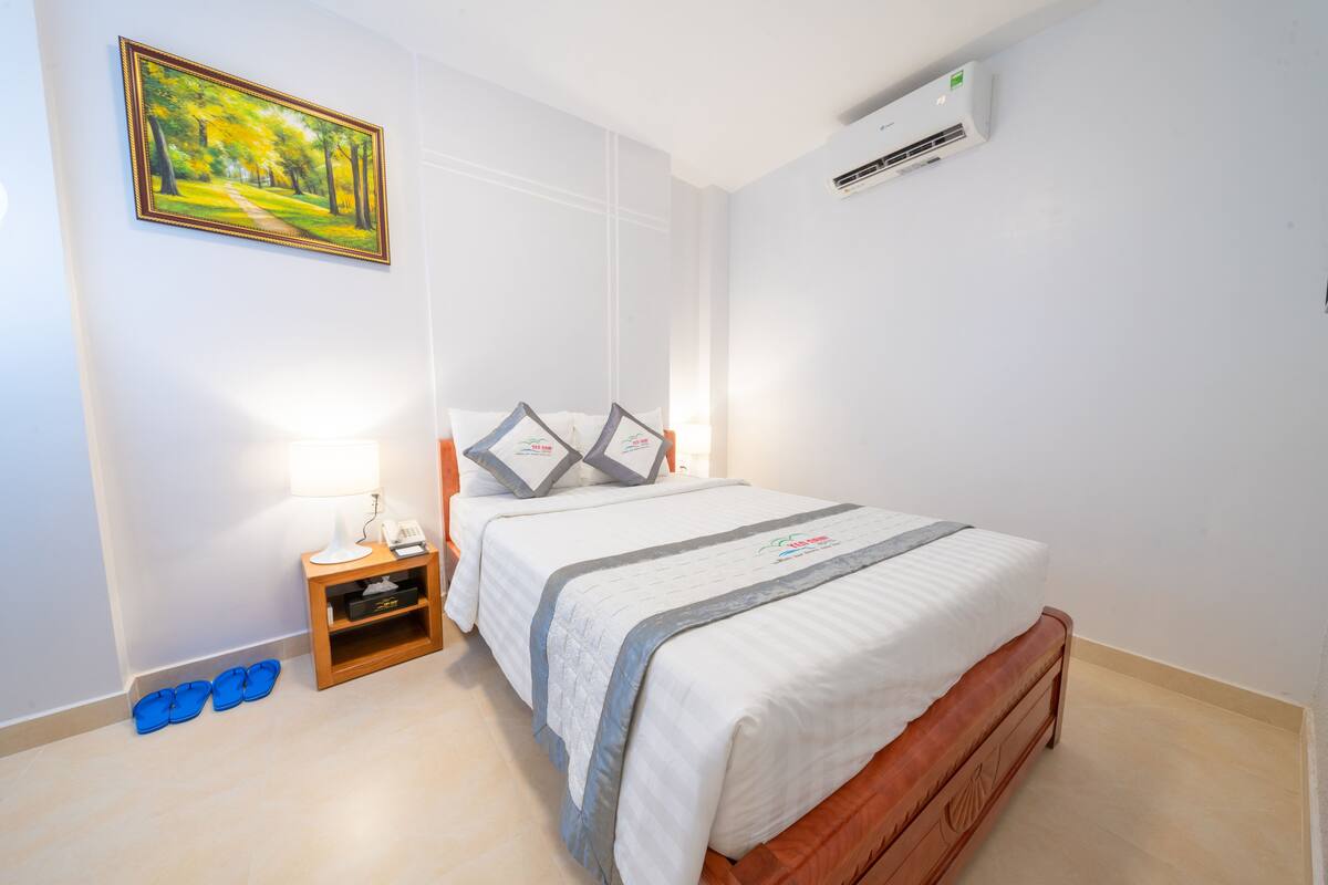 A neatly arranged bedroom with a bed, bedside table, lamp, and a painting on the wall.