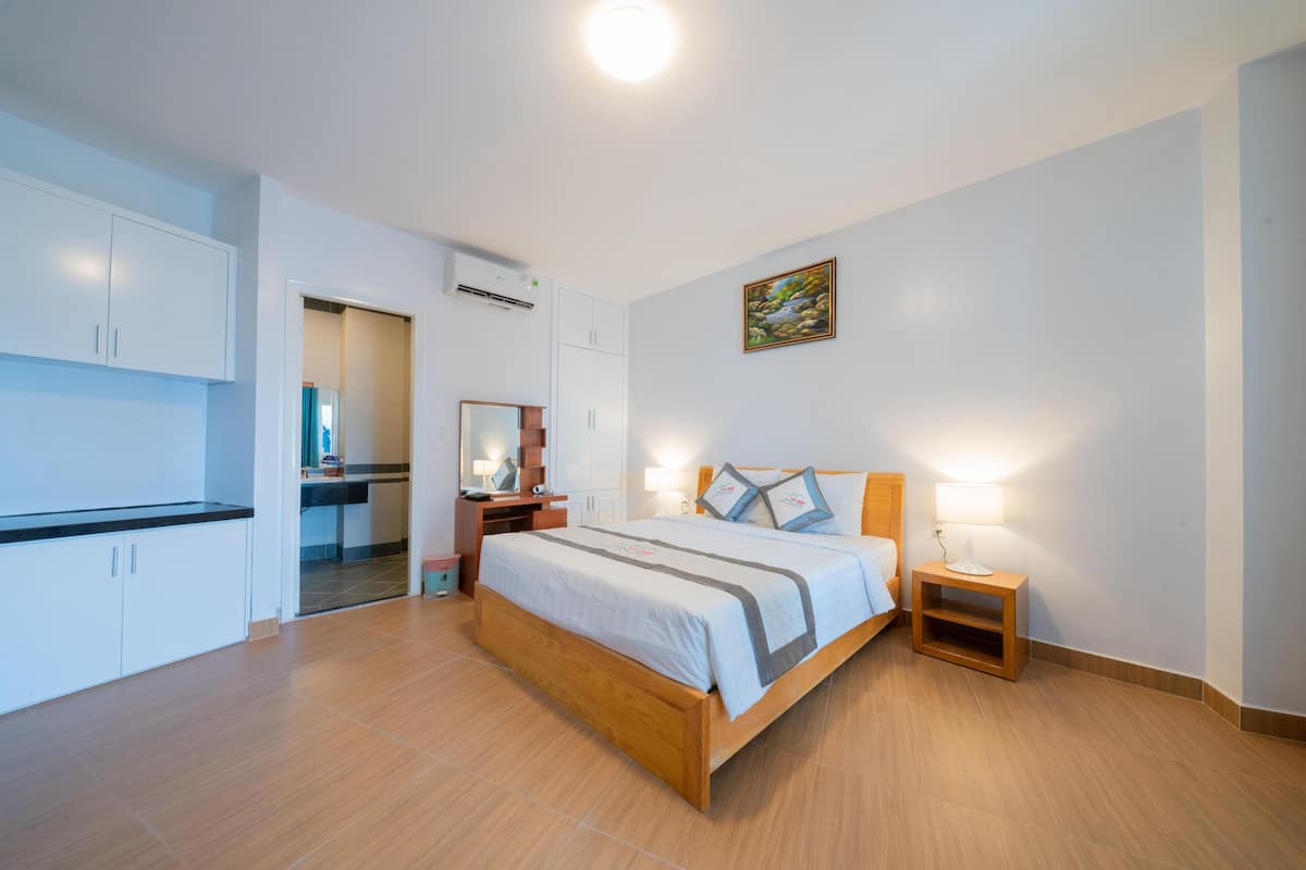 A bedroom with a wooden bed, bedside tables, a nightstand, a mirror, and a painting on the wall.