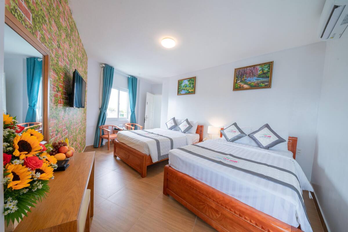 A hotel room with two beds, a wooden desk, a mirror, and a wall with a floral pattern.