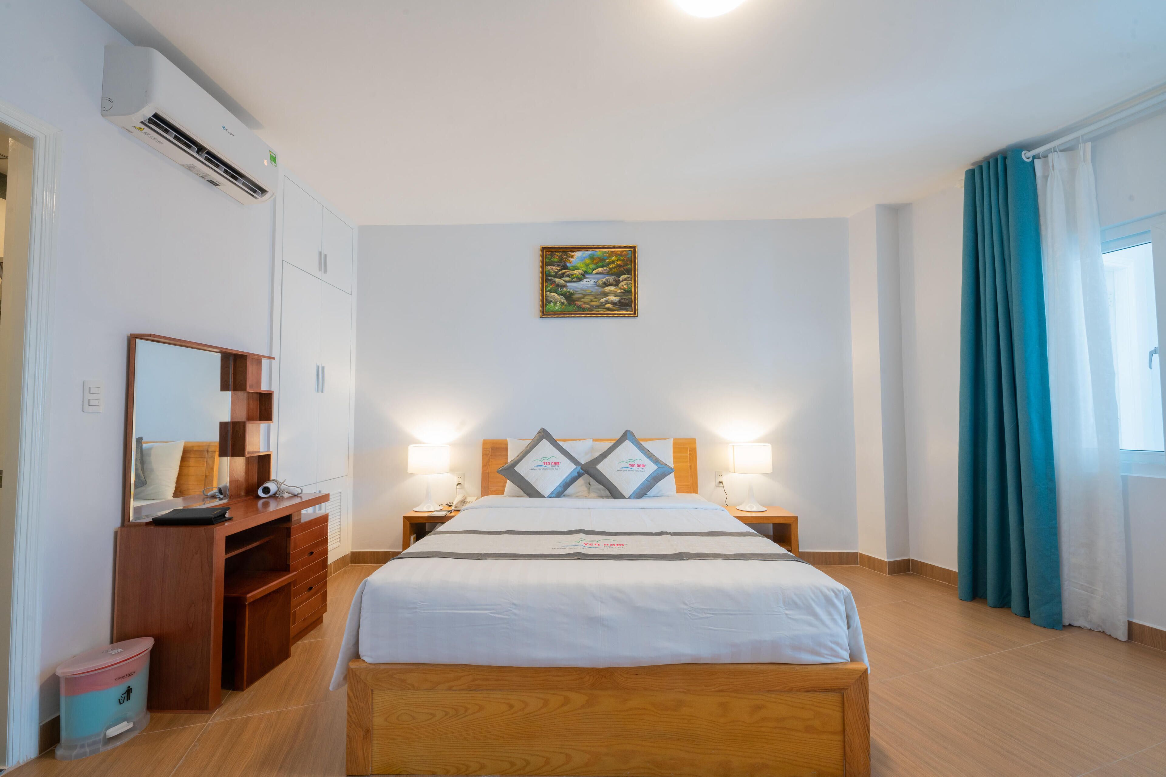 Une chambre d’hôtel avec un lit en bois, un bureau doté d’un miroir, une petite poubelle et un tableau accroché au mur.