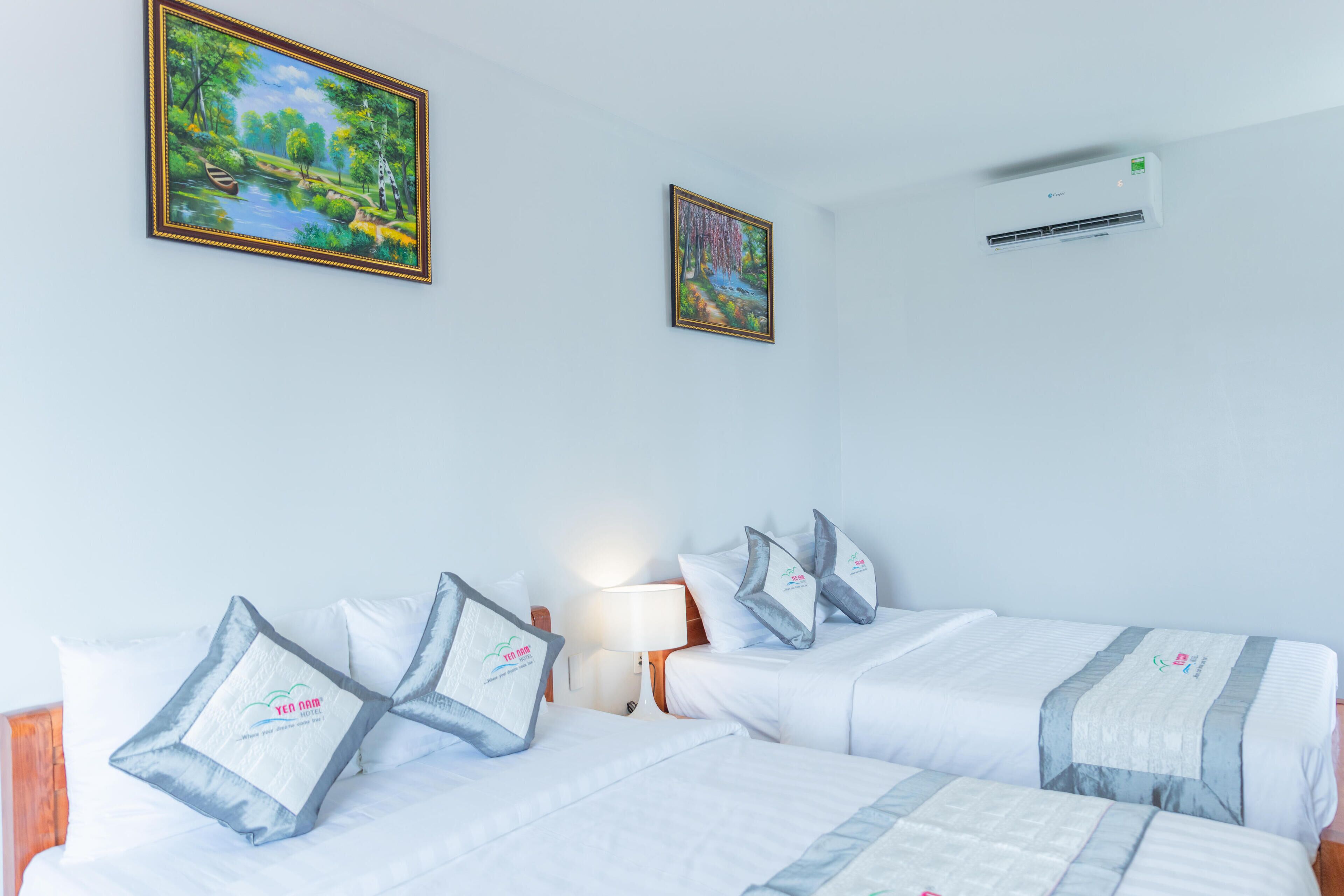 A hotel room with two beds, a nightstand, a lamp, and two paintings on the wall.