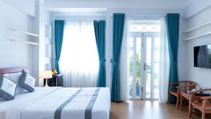 Hotelkamer met een bed, bureau, stoel, televisie en balkon met gordijnen.
