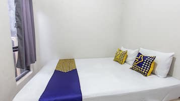 A single bed with a white mattress, a blue bedspread, and three decorative pillows with yellow and blue patterns.