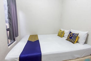 Una cama individual con colchón blanco, colcha azul y tres almohadas decorativas con diseños azules y amarillos.