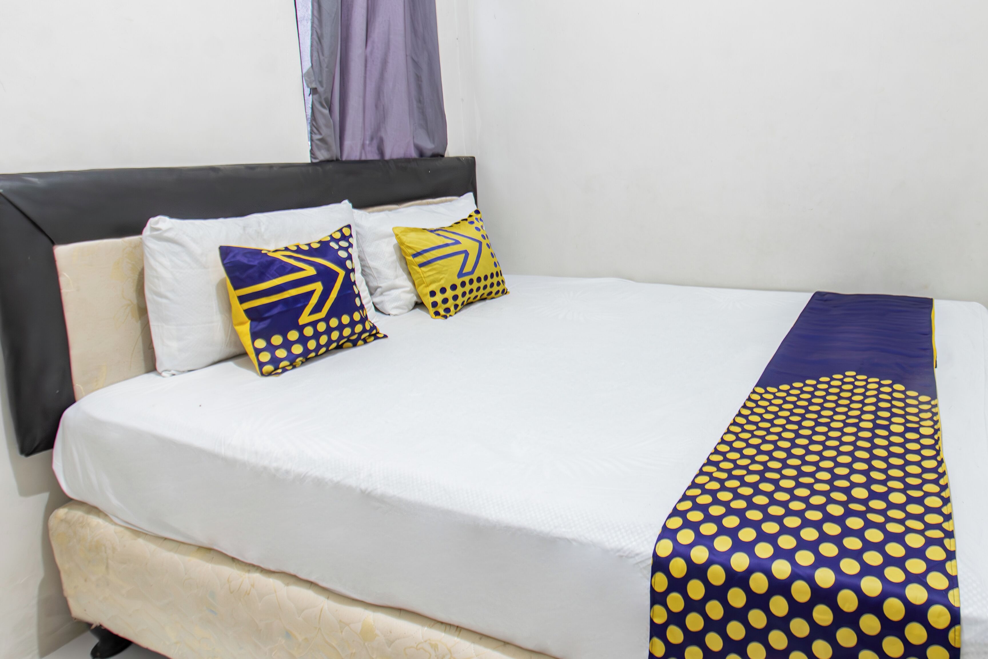 A bed with a white mattress, a grey headboard, and decorative pillows with geometric patterns.
