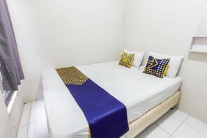 A small, single-bed room with a white bedspread, two pillows with geometric patterns, and a blue accent pillow. - Hotel O Penginapan Melati Tanjung Near Kantor Pengamat Pengairan Tanjung (Tanjung)