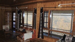 A wooden interior with a sofa, a table, and large windows offering a mountain view. - AJ Himalayan Homestay (Kumharsain)