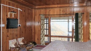 A wooden cabin room with a bed, a TV mounted on the wall, and a window with a view of the mountains. - AJ Himalayan Homestay (Kumharsain)