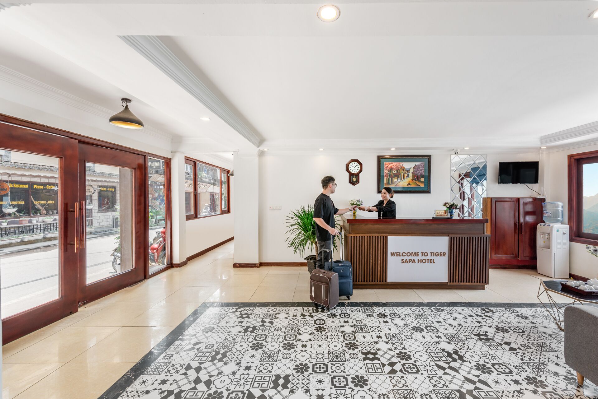 Zona de recepción de un hotel con mostrador, un reloj, un cuadro enmarcado y dispensador de agua.