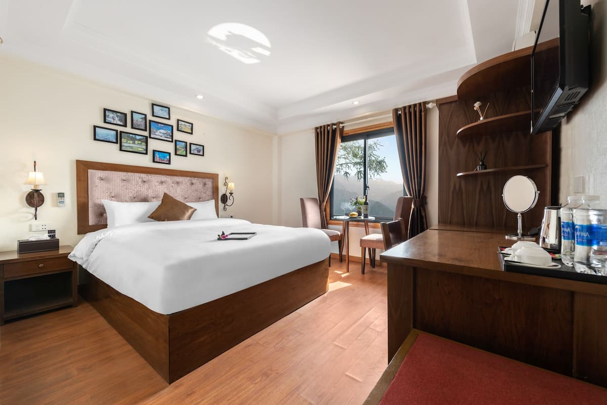 Une chambre d’hôtel avec un grand lit, un bureau, une chaise, une télévision et une fenêtre donnant sur les montagnes.