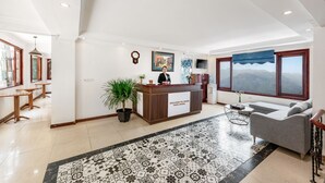 A hotel lobby with a reception desk, a sofa, a large window with a mountain view, and a patterned floor. - Tiger Sapa Hotel (Sa Pa)