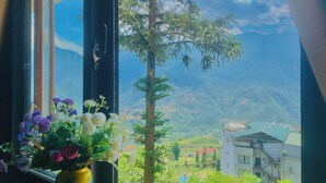 A window with a view of a mountain landscape, a tree, and a building with a green roof. - Tiger Sapa Hotel (Sa Pa)