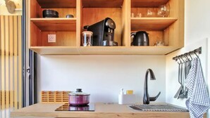 Una cocina compacta con un refrigerador blanco, estantes de madera arriba y un lavamanos con un perchero.