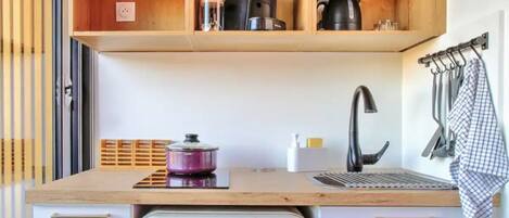 A compact kitchen with a white refrigerator, wooden shelves above, and a sink with a towel rack.