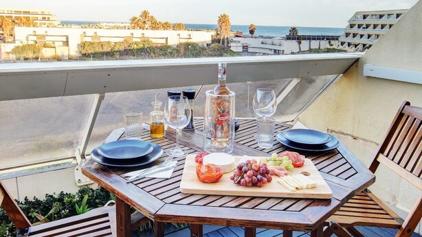 Mesa lista para comer con vista al océano, una botella de licor y diversos bocadillos.