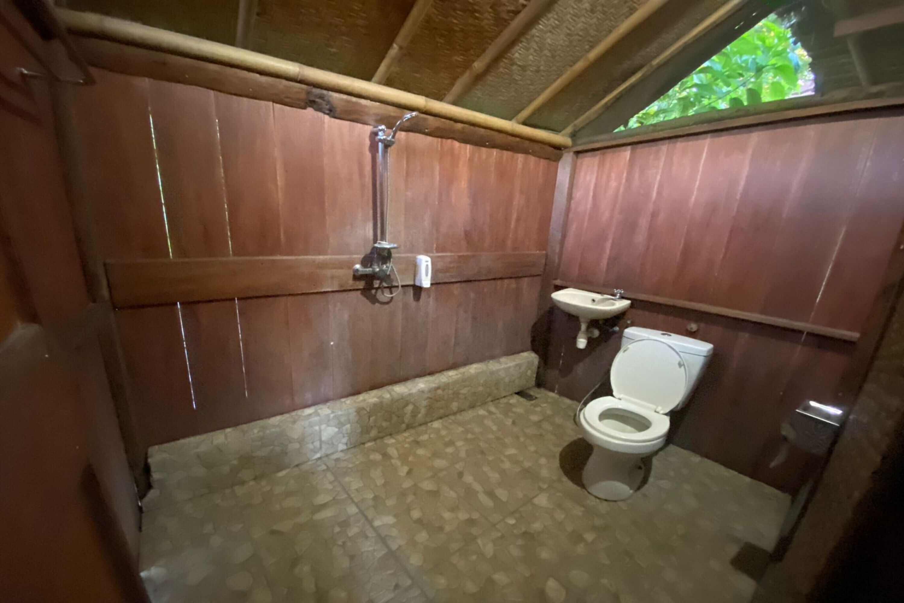 A small, wooden-paneled bathroom with a toilet and a sink.