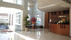 Uma área de recepção de hotel com um balcão de madeira, um candelabro e um vaso de planta.